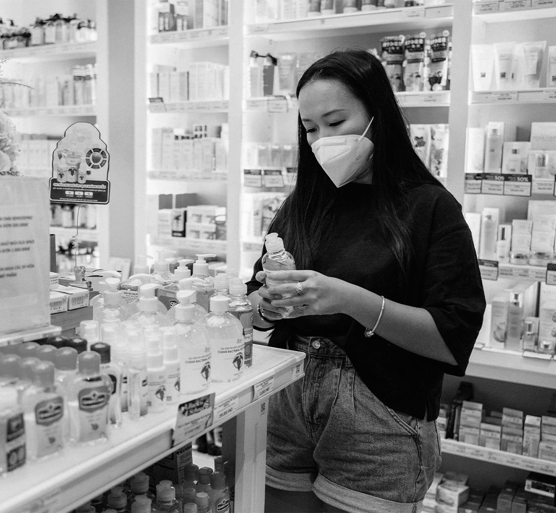 a woman wearing a mask in a pharmacy holding pharmaceutical products